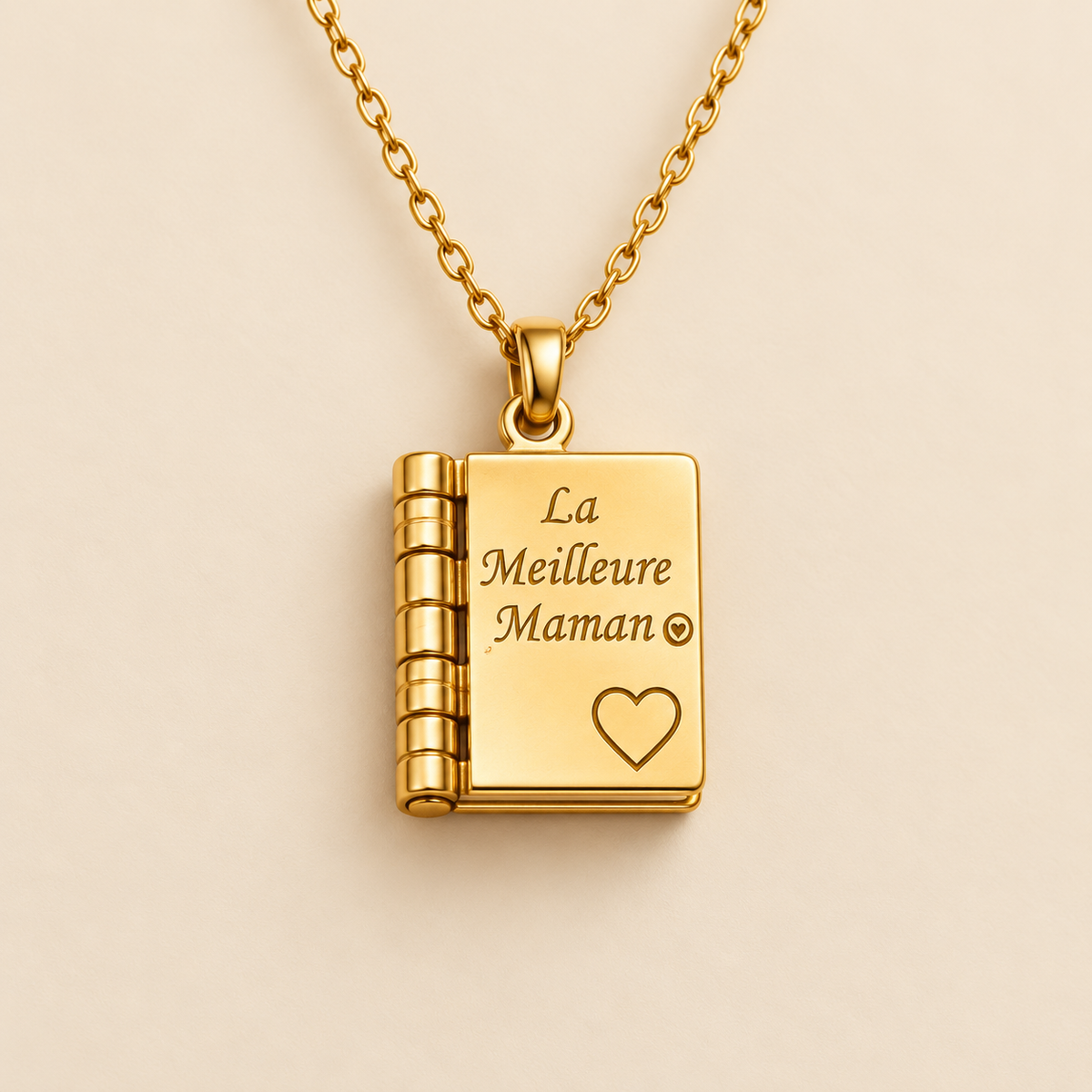 Mise en scène illustrative du pendentif livre « La Meilleure Maman » sur fond champagne, réalisée à partir du visuel fourni.